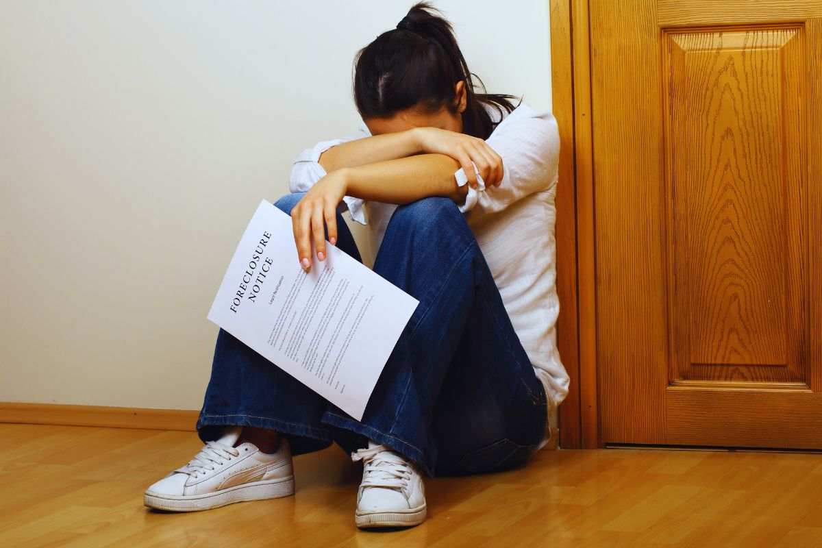 Ragazza rannicchiata a terra con in mano una notifica di pignoramento