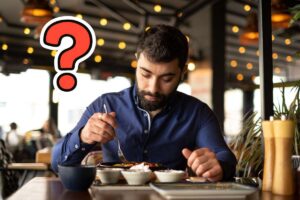 Una persona che pranza da sola in un ristorante ed un punto interrogativo in alto a sinistra