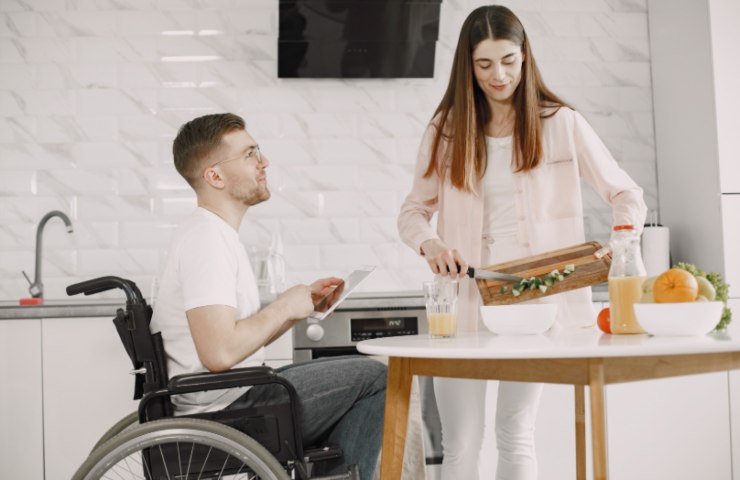 ragazzo sulla sedia a rotelle e accanto una donna che cucina