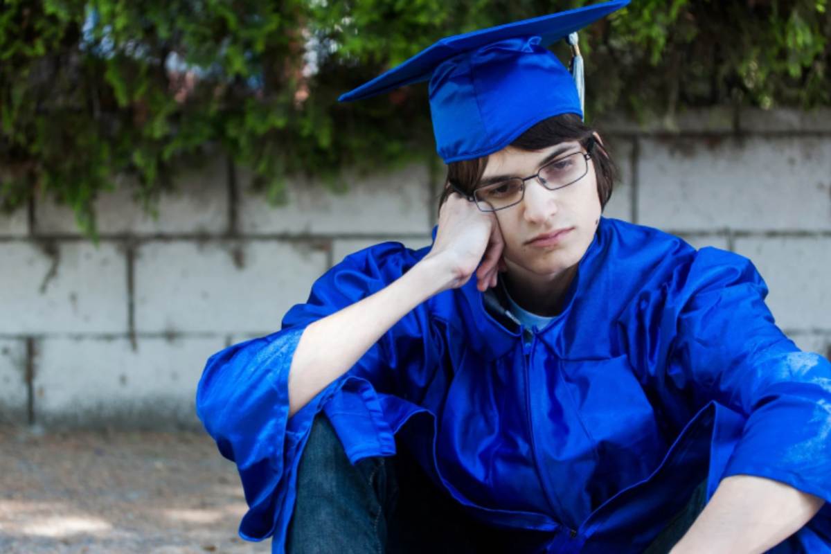 ragazzo triste appena laureato seduto sul marciapiede